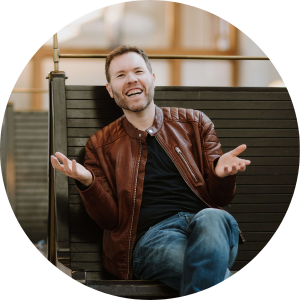 Ron Ben-Joseph, executive public speaking coach, laughing with his hands open mid-gesture on a station bench